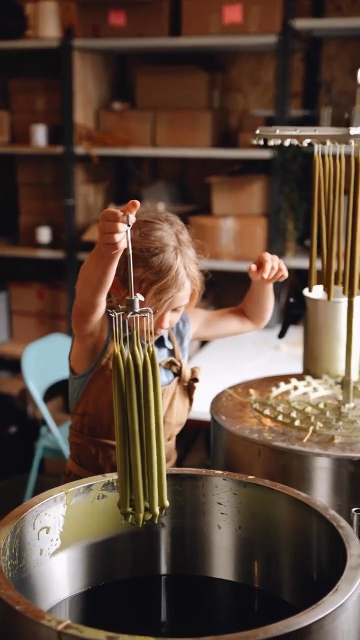 Frame from the candle-dipping film: fresh-dipped organic beeswax candles lifted from the wax